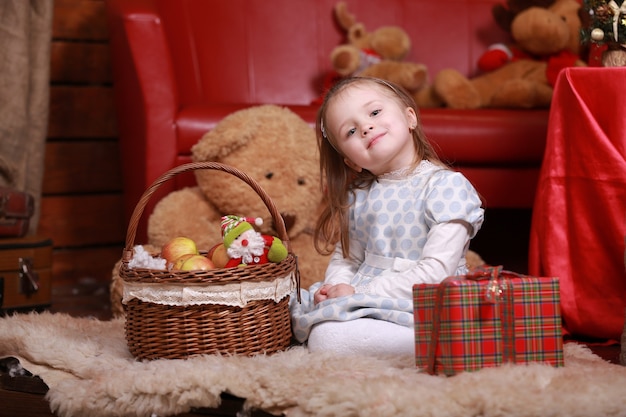 Petite fille en robe à pois blancs s'amusant dans le studio de Noël. Arbre de Noël, ours en peluche et panier avec des cadeaux sur le devant.