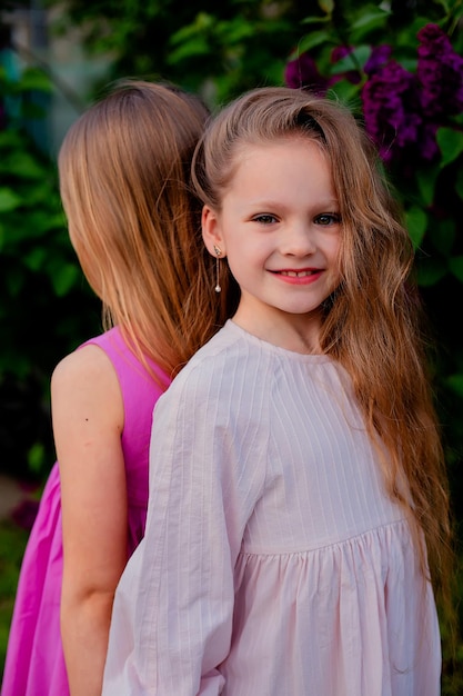 Une petite fille avec une robe rose se tient derrière une fille avec une fleur violette derrière elle.