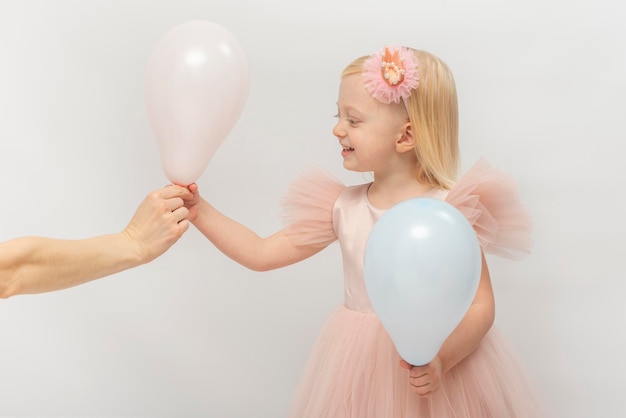 Petite fille en robe rose souriante prend le ballon de la main féminine Petite princesse blonde sur fond blanc Birhtday célébrer