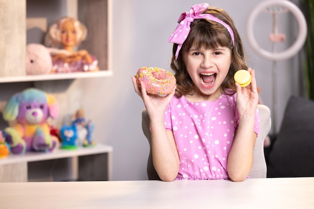 Petite fille en robe rose tenant un macaron et un beignet dans les mains par le visage adolescente de l'école