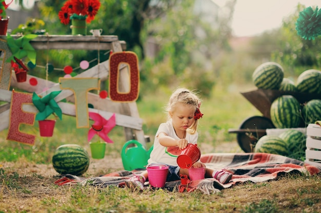 Petite fille en robe rouge est assise dans un jardin près d'une récolte de pastèques