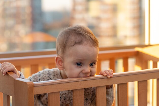 une petite fille ronge tristement le bord de son berceau avec ses dents en attendant ses parents