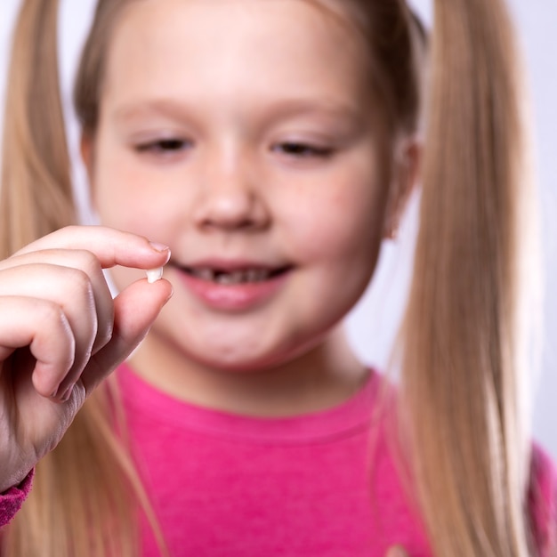 Petite fille en rose tient une dent de lait tombée