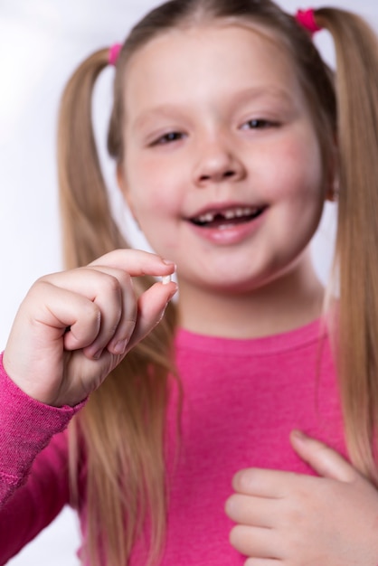 Petite fille en rose tient une dent de lait tombée