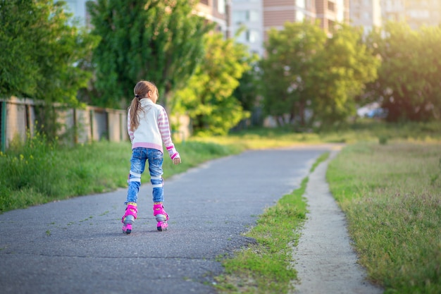 Une petite fille roule sur des patins à roulettes roses sur l'asphalte