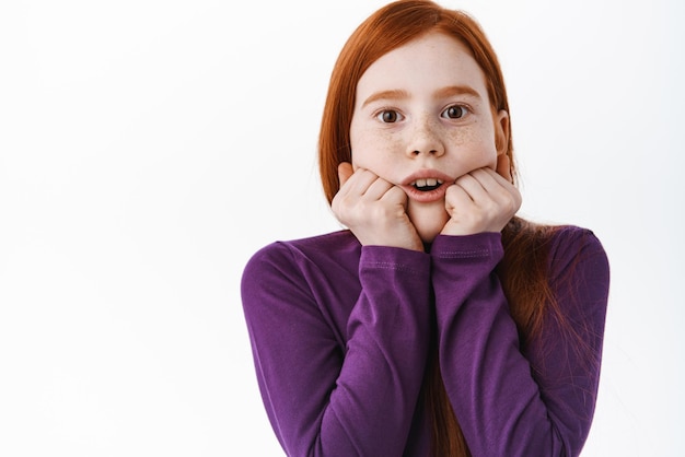 Une petite fille rousse fascinée regarde avec intérêt et émerveillement quelque chose à couper le souffle et impressionnant debout étonné sur fond blanc