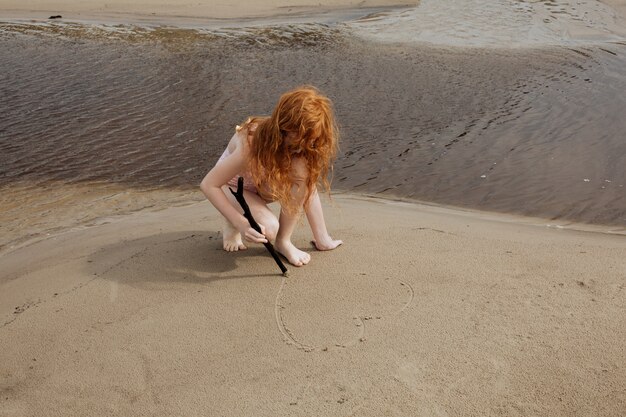 Petite fille rousse jouant sur une plage