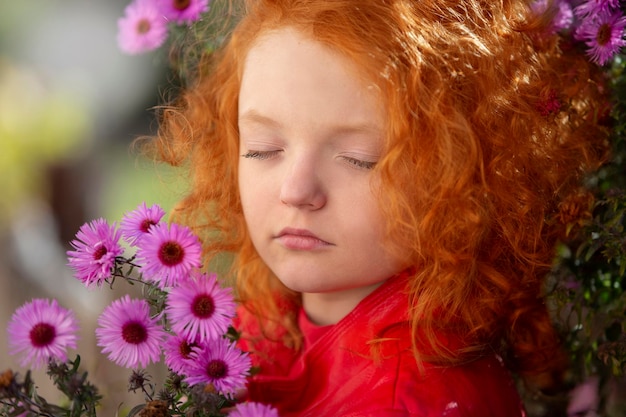 La petite fille rousse avec les yeux fermés tient un bouquet des chrysanthèmes pourpres
