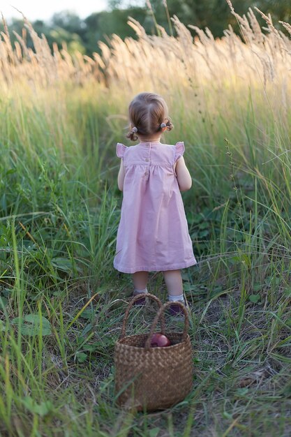 Une petite fille sur la route dans un champ de blé au coucher du soleil, marchant le long du chemin dos à la caméra, va au loin.
