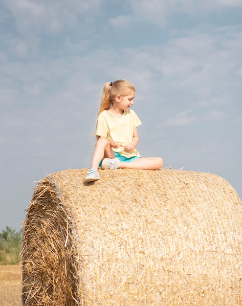 Petite fille s'amusant dans un champ de blé un jour d'été. Enfant jouant au champ de balles de foin pendant la récolte.