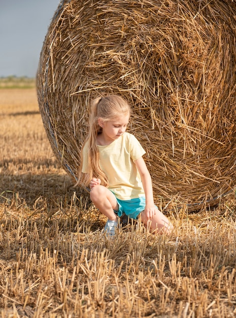 Petite fille s'amusant dans un champ de blé un jour d'été. Enfant jouant au champ de balles de foin pendant la récolte.