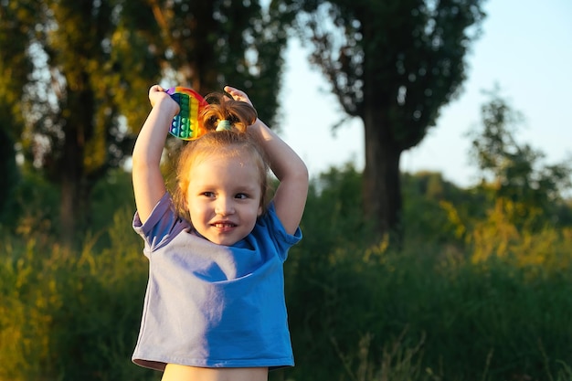 une petite fille s'amuse lors d'une promenade en dehors de la ville dans ses mains elle a un jouet pop-it antistress