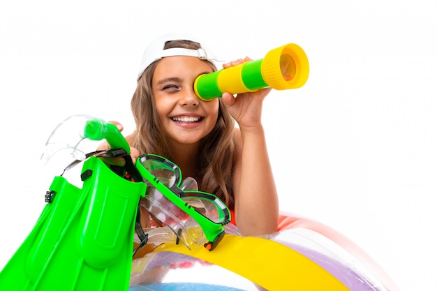 La petite fille s'appuie sur une grande balle gonflable de couleur plaie, tient dur, un masque de natation et se penche sur un jouet sous-pipe et sourit, isolé sur fond blanc