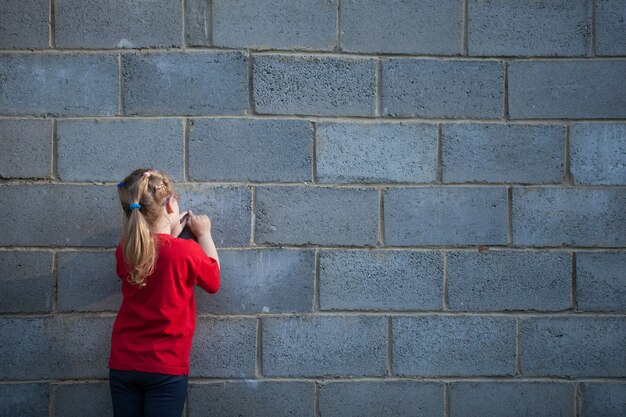 La petite fille s'appuie sur un mur de briques grises