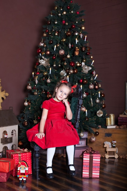 Petite fille s'asseoir dans la salle vivin près de l'arbre de Noël et des cadeaux