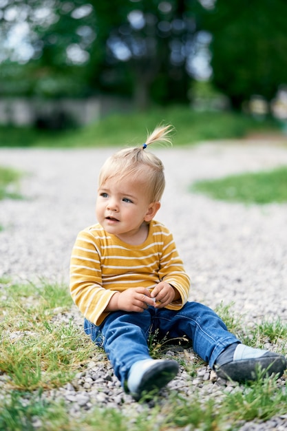 La petite fille s'assied sur un chemin de gravier et tient un petit caillou dans sa main