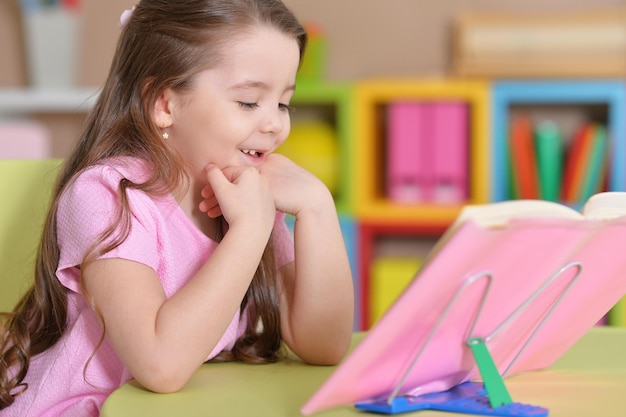 La petite fille s'assied à la table et lit un livre