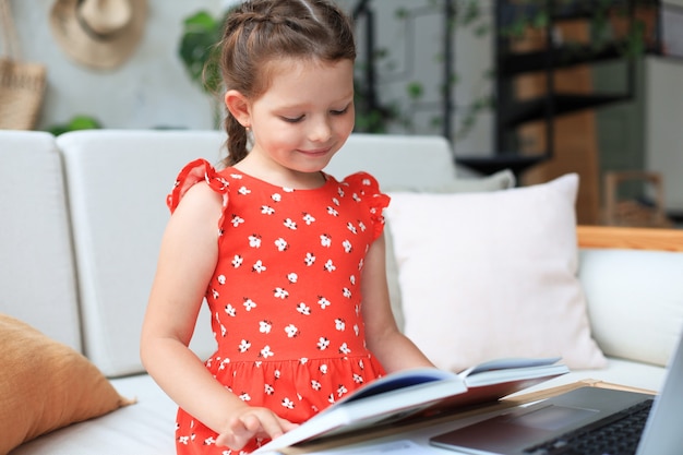 Une petite fille s'assoit au desl à la maison et fait ses devoirs, étudie elle-même le matériel, lit un livre. Le concept de l'enseignement à distance.