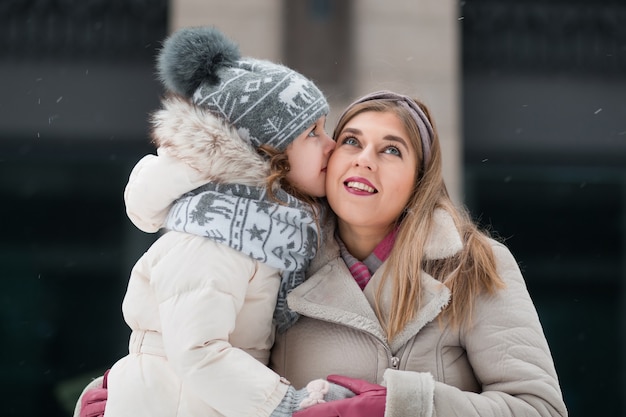 Photo petite fille s'embrassant avec sa mère dans la ville d'hiver