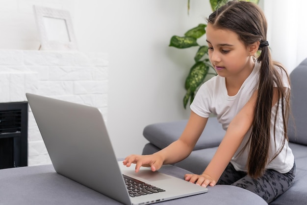 Petite fille s'ennuie avec un ordinateur portable à la maison. Enfant mignon faisant ses devoirs sur ordinateur. Concept moderne d'éducation, de communication et de technologie en ligne, espace de copie.