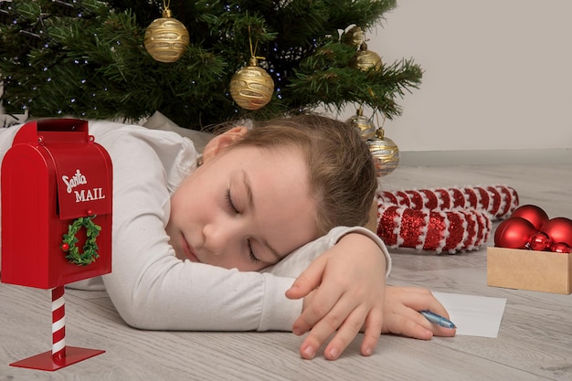 Une petite fille s'est endormie sous le sapin de noël en écrivant une lettre au père noël