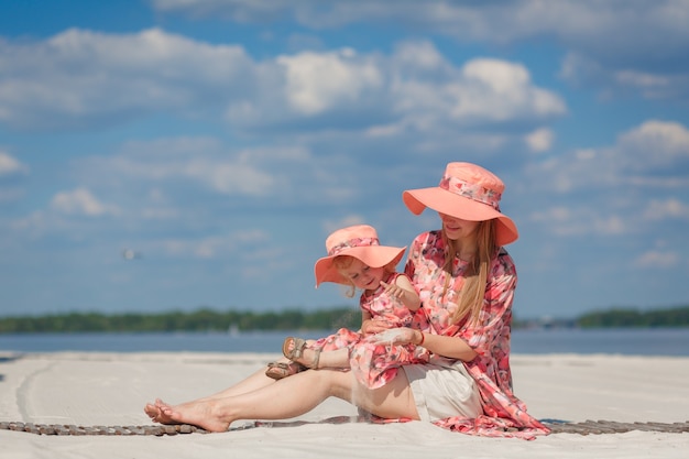 Une petite fille avec sa mère dans de belles robes d'été assorties joue dans le sable sur la plage. Look familial élégant.