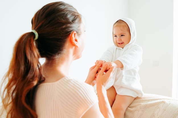 Petite fille sa mère joue assise sur le canapé mère tient les mains de l'enfant les tourne dans des directions différentes