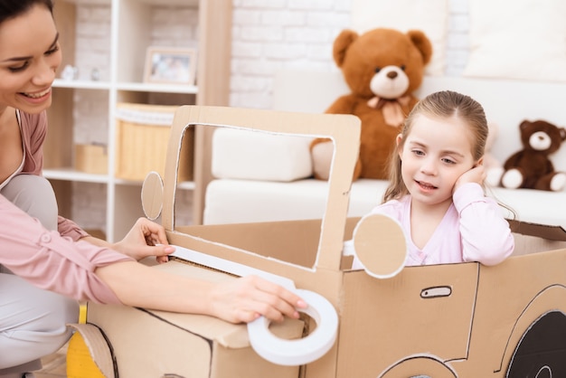 Une petite fille avec sa mère joue avec une petite voiture.