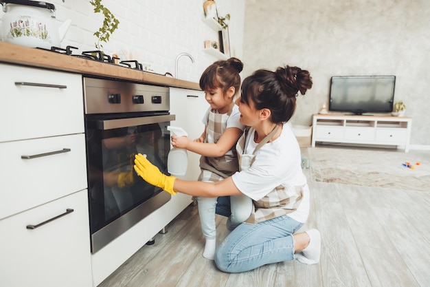 Une petite fille et sa mère nettoient la cuisine une femme et un enfant essuient le four dans la cuisine ménage aidant maman