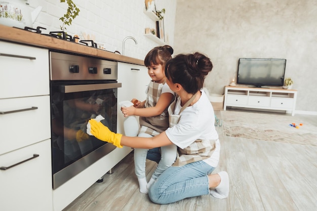 Une petite fille et sa mère nettoient la cuisine une femme et un enfant essuient le four dans la cuisine ménage aidant maman