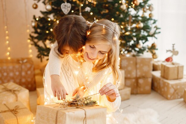 La petite fille et sa mère sont assises près de l'arbre de Noël et s'embrassent.