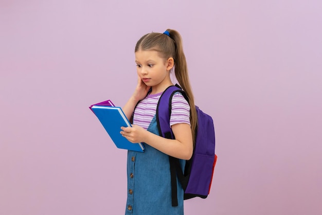 Une petite fille avec un sac à dos scolaire a l'air très surprise par les livres. une écolière avec des manuels dans ses mains. fond isolé.