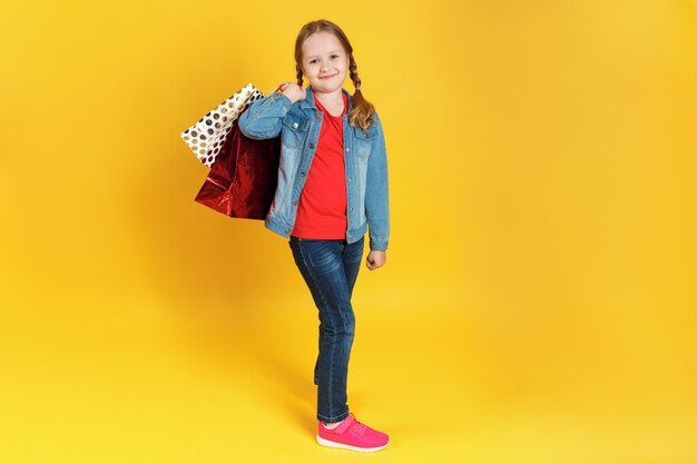 Petite fille avec des sacs sur fond jaune