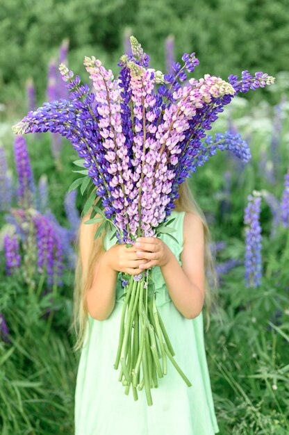 Petite fille sans visage avec bouquet de lupins en fleurs
