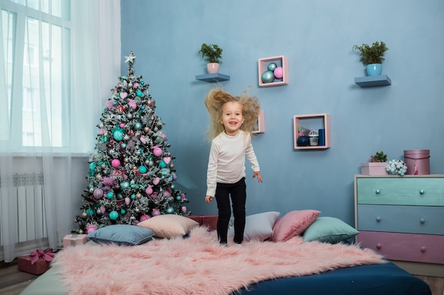 Petite fille saute sur le lit contre l'arbre de Noël