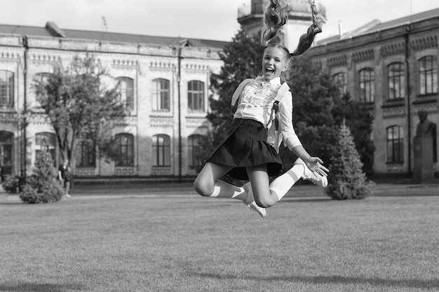 Petite fille saute avec sac à dos heureux d'être ici souvenirs d'enfance heureux fin de leçon retour à l'école enfant étude dans le parc se détendre sur l'herbe verte avec sac d'école concept d'éducation clé du succès