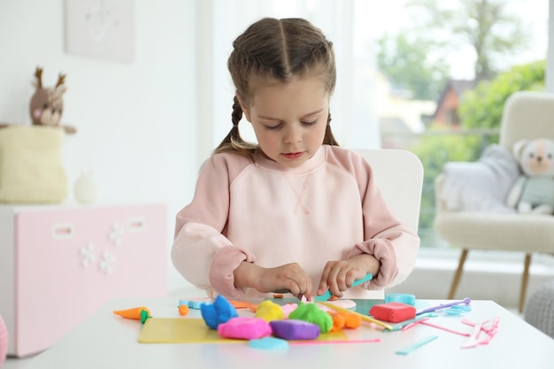 Petite fille sculptant avec de la pâte de jeu à la table à la maternelle