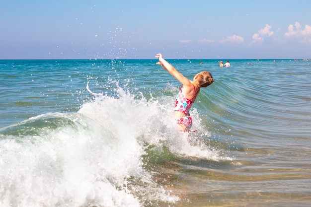 Une petite fille se baigne dans les vagues de la mer. Du plaisir et du plaisir pendant les vacances d'été.