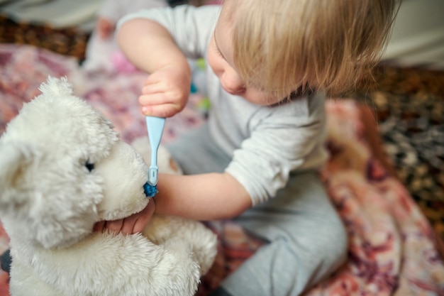 Petite fille se brosse les dents avec un ours en peluche ambiance maison