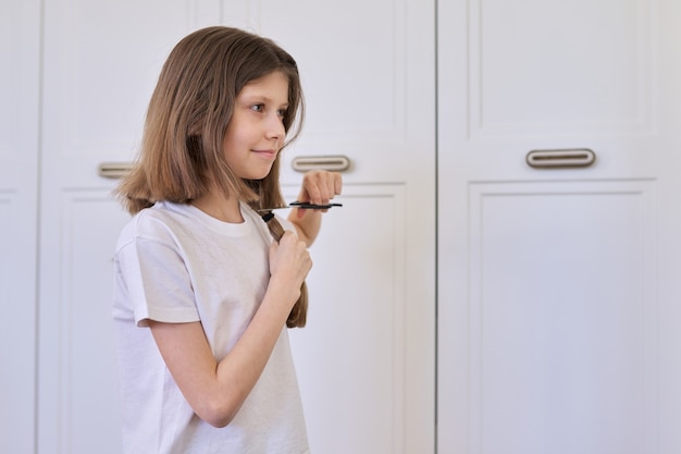 Une petite fille se coupe les cheveux avec des ciseaux, une petite belle coiffeuse drôle, une styliste, une coiffeuse de salon à la maison, un espace de copie