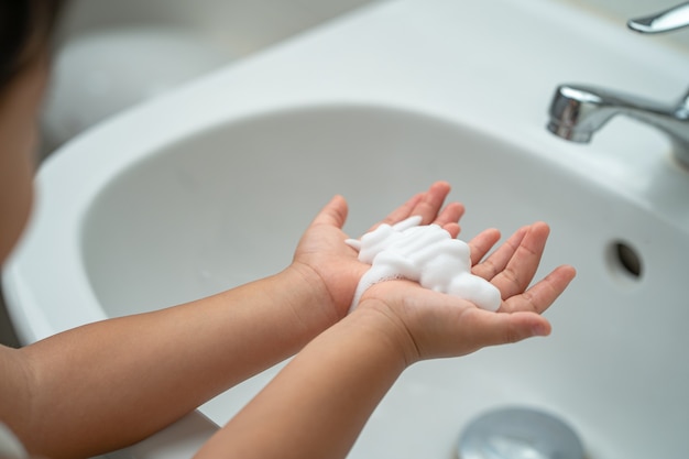 Petite fille se lavant les mains pour prévenir les virus, les germes et les bactéries au lavabo du lavabo