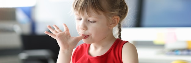 Petite fille se léchant les doigts devant un verre de crème glacée. Concept de nourriture saine et savoureuse pour les enfants