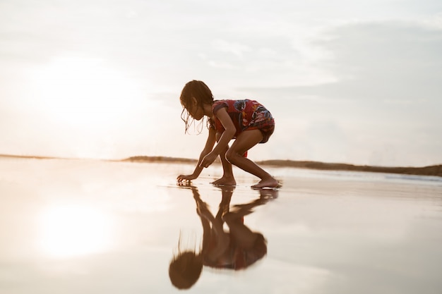 Petite fille se pencha et jouant du sable sur la plage