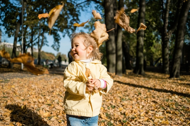 Petite fille se promène dans le parc à l'automne et jette des feuilles.