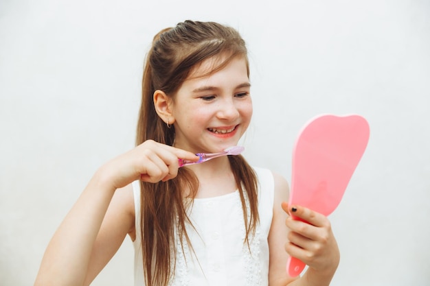 Petite fille se regarde dans le miroir et se brosse les dents sur fond blanc Hygiène et soins dentaires