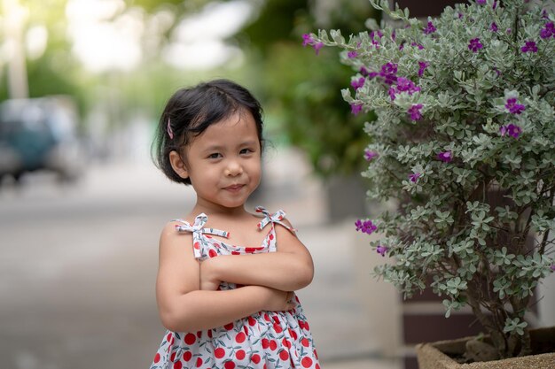 Une petite fille se tient devant une plante avec une fleur rose en arrière-plan.