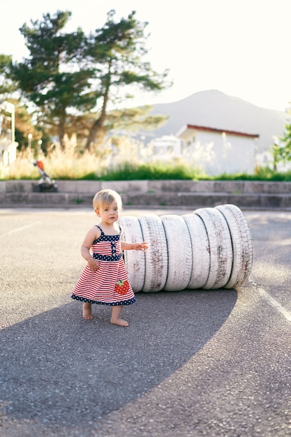 La petite fille se tient près des pneus blancs dans le parking