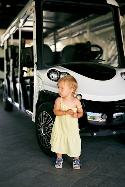 Une petite fille se tient près d'une voiturette de golf à six places dans le parking