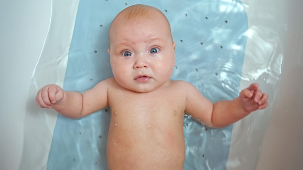 La petite fille se trouve dans l'eau du bain et regarde directement les parents