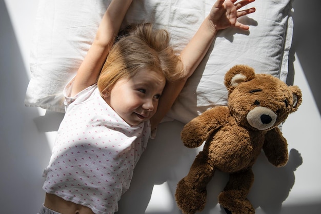 Petite fille se trouve avec un ours en peluche vue de dessus mise à plat